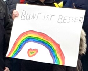 ein Regenboben auf einem Papierplakat, darüber 'Bunt ist Besser', im Bogen ein ebenfalls buntes Hert